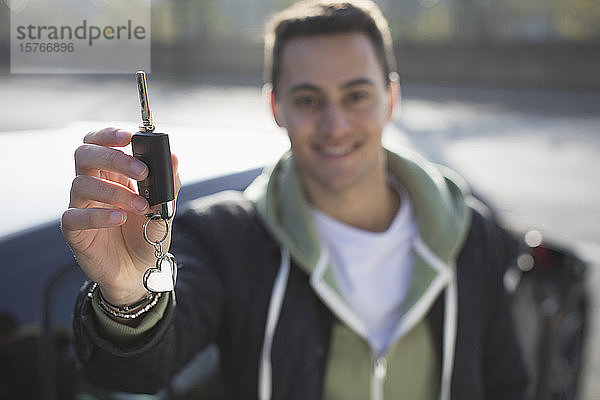 Porträt eines lächelnden  selbstbewussten jungen Mannes mit neuem Autoschlüssel