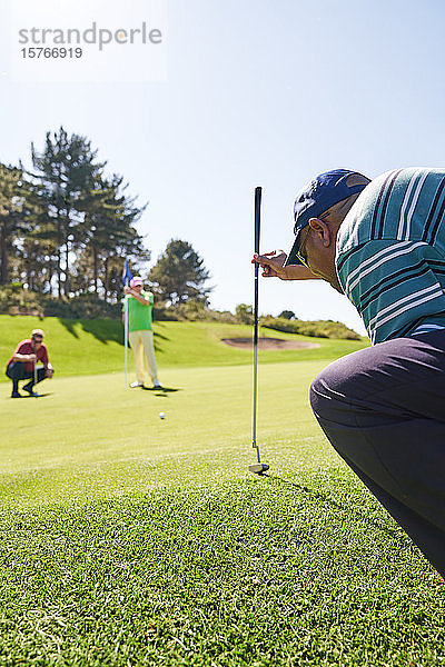 Männlicher Golfer bereitet sich auf einen Schlag auf dem sonnigen Putting Green vor