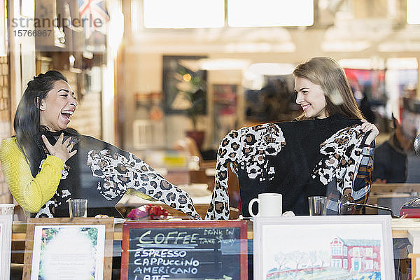 Glückliche junge Freundinnen mit passenden Pullovern im Schaufenster eines Cafés