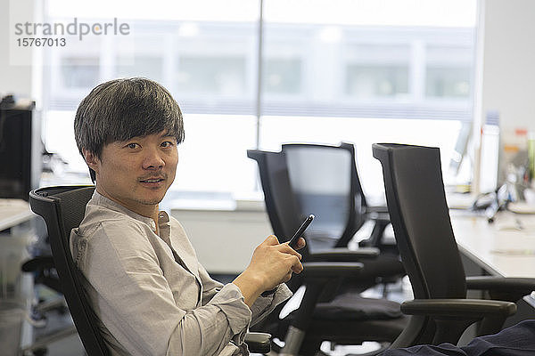 Porträt selbstbewusster Geschäftsmann mit Smartphone im Büro