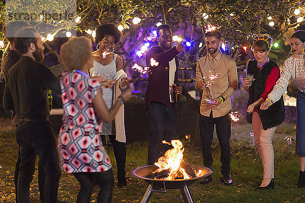 Freunde mit Wunderkerzen um eine Feuerstelle bei einer Gartenparty