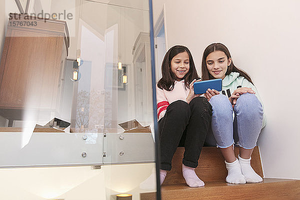 Schwestern benutzen Smartphone auf der Treppe zu Hause