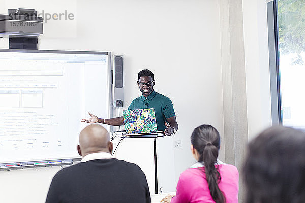 Männlicher Community-College-Lehrer  der an einem Laptop und einer Projektionsfläche im Klassenzimmer Unterricht erteilt