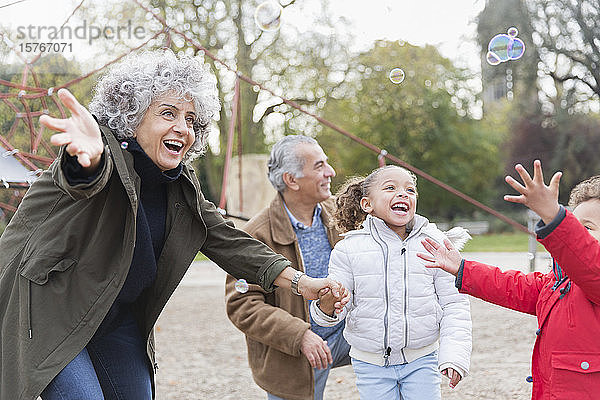 Verspielte Großeltern und Enkelkinder spielen mit Seifenblasen im Park