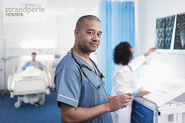 Porträt eines selbstbewussten  lächelnden Arztes  der ein digitales Tablet in einem Krankenhauszimmer benutzt