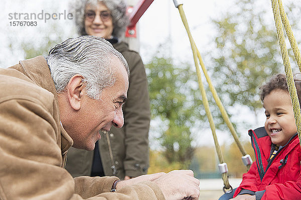 Großvater spielt mit seinem Enkel auf einer Schaukel auf dem Spielplatz