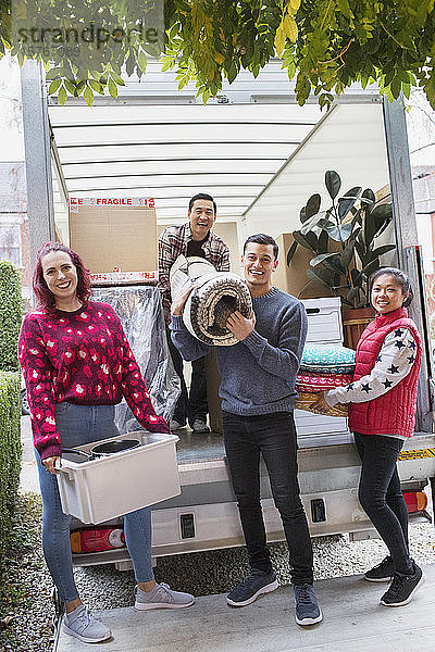 Porträt glücklicher Freunde beim Entladen von Habseligkeiten aus einem Umzugswagen