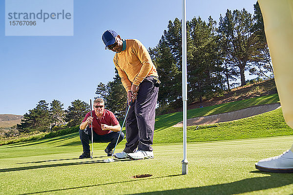 Männlicher Golfer beim Einlochen auf dem sonnigen Golfplatz Putting Green