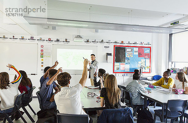 Gymnasiallehrer fordert Schüler mit erhobenen Händen während des Unterrichts im Klassenzimmer auf
