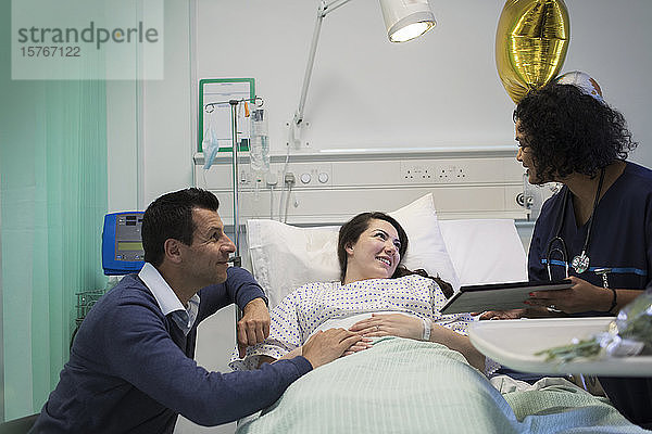 Arzt mit digitalem Tablet bei der Visite  Gespräch mit Paar im Krankenhauszimmer