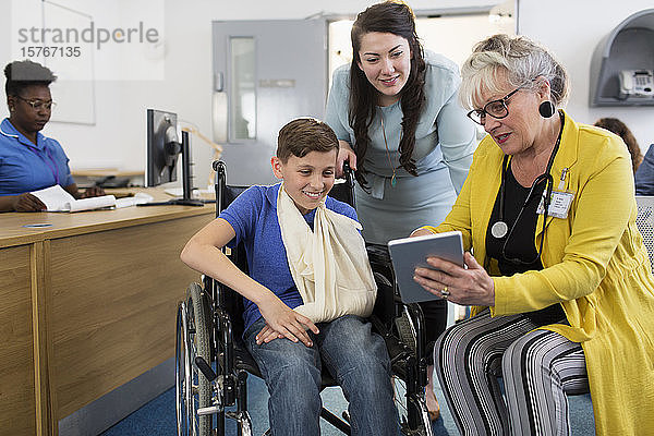 Ärztin mit digitalem Tablet im Gespräch mit einer Mutter und einem kleinen Patienten im Rollstuhl in der Kliniklobby