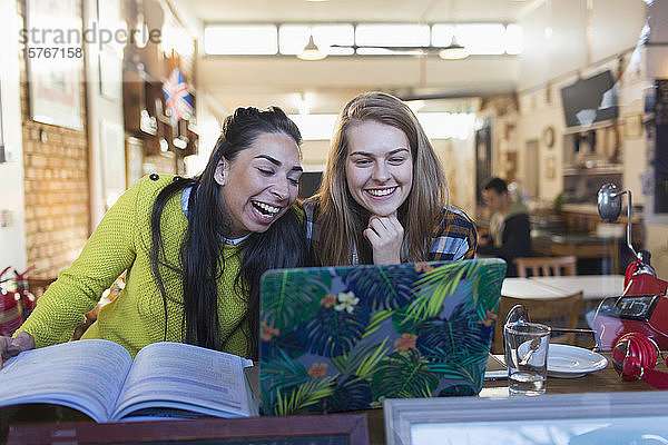 Fröhliche  lachende junge Studentinnen mit Laptop in einem Caféfenster