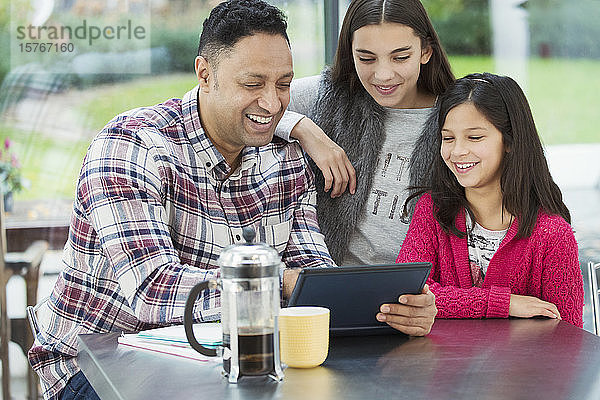 Ein glücklicher Vater und seine Töchter benutzen ein digitales Tablet in der morgendlichen Küche