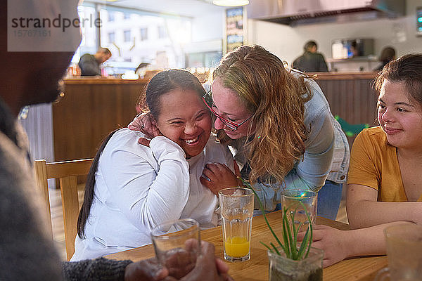 Fröhliche Mentorin und junge Frauen mit Down-Syndrom lachen im Cafe
