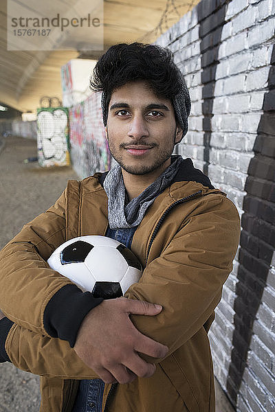 Porträt selbstbewusster junger Mann mit Fußball in städtischem Tunnel