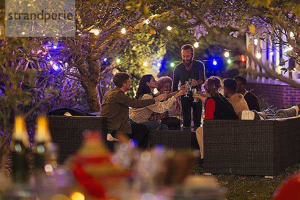 Freunde trinken unter Bäumen mit Lichterketten bei einer Gartenparty