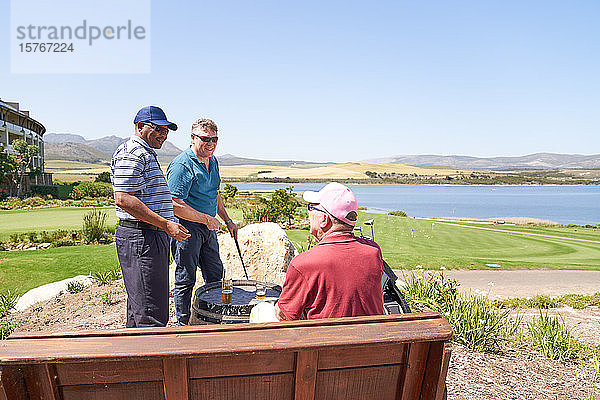 Männliche Golffreunde unterhalten sich beim Biertrinken auf einer sonnigen Golfplatzterrasse