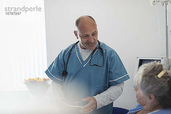 Arzt mit digitalem Tablet bei der Visite  Gespräch mit älterem Patienten im Krankenhauszimmer