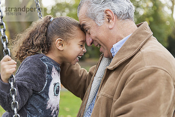 Verspielter  liebevoller Großvater und Enkelin auf einer Schaukel auf dem Spielplatz