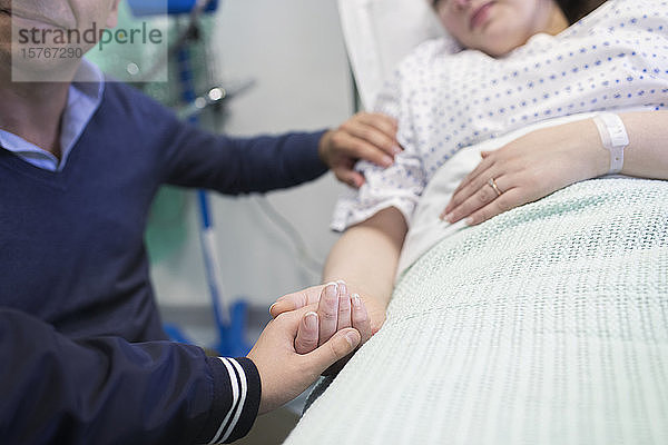 Zärtlicher Sohn hält die Hände seiner Mutter  die im Krankenhausbett ruht
