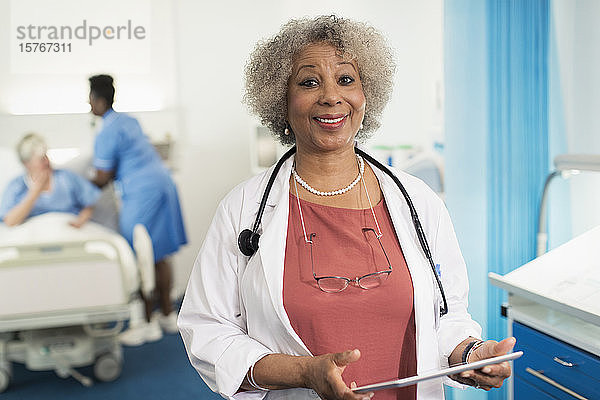 Porträt einer selbstbewussten Ärztin  die ein digitales Tablet in einem Krankenhauszimmer benutzt