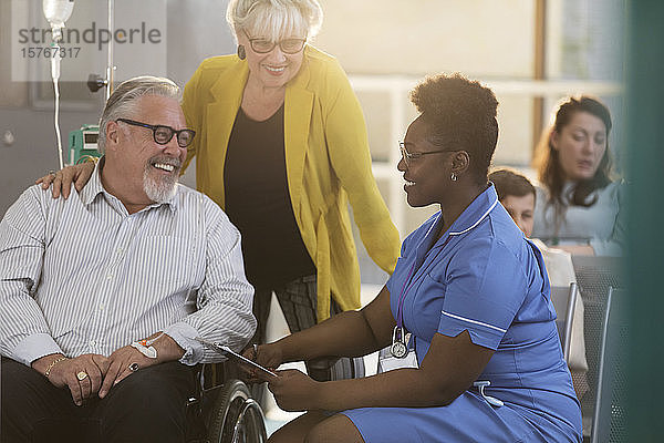 Weibliche Krankenschwester im Gespräch mit einem älteren männlichen Patienten im Rollstuhl in der Kliniklobby