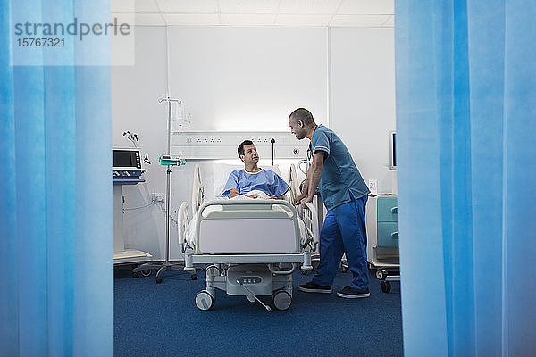 Krankenpfleger im Gespräch mit einem Patienten  der sich im Krankenhauszimmer ausruht