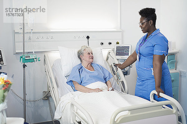 Weibliche Krankenschwester im Gespräch mit einem älteren Patienten in einem Krankenhauszimmer