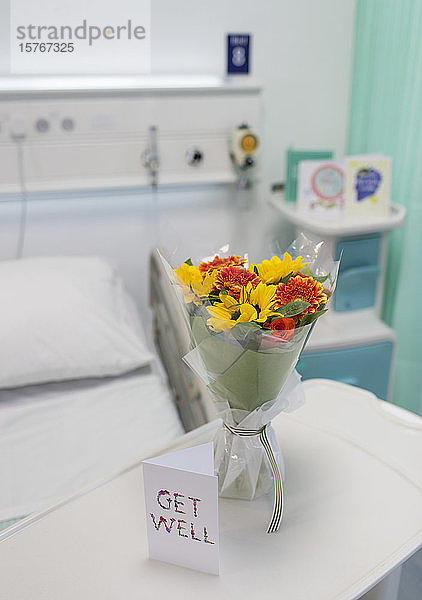 Blumenstrauß und Genesungskarte auf einem Tablett in einem leeren Krankenhauszimmer