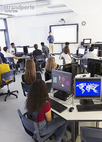 Schüler der Mittelstufe an Computern hören dem Lehrer auf der Projektionsfläche im Klassenzimmer zu