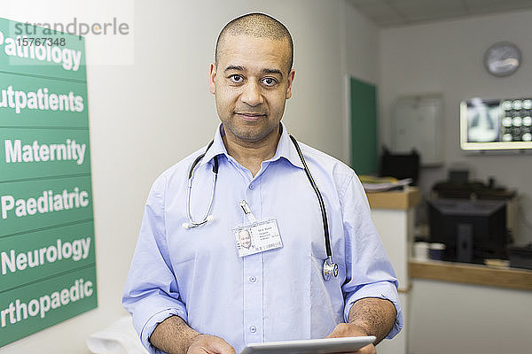 Porträt selbstbewusster männlicher Arzt mit digitalem Tablet in einem Krankenhauskorridor