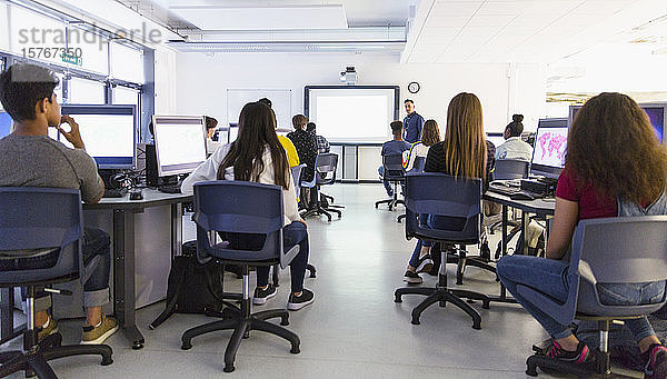 Schüler der Mittelstufe an Computern  die den Lehrer auf der Projektionsfläche im Klassenzimmer beobachten