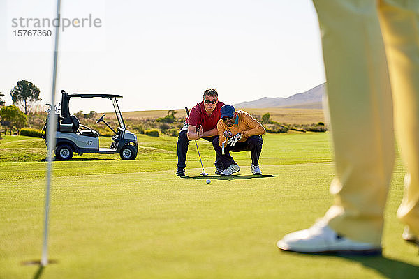 Männliche Golfer planen den Putt auf sonnigen Golfplätzen