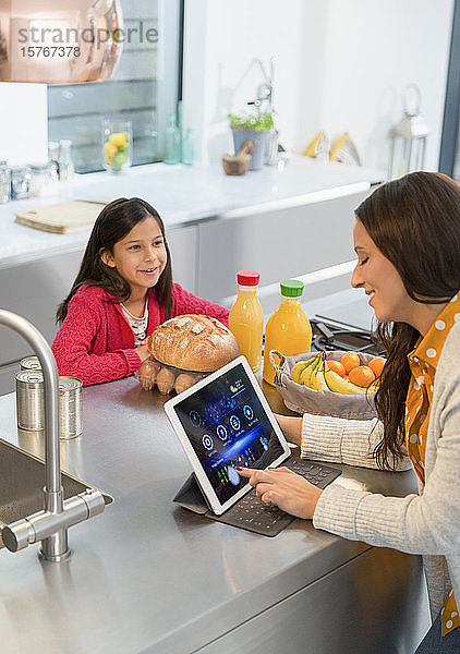 Tochter beobachtet Mutter bei der Nutzung eines digitalen Tablets in der Küche