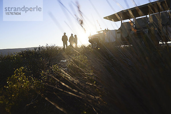 Silhouette Safaritour Gruppe und Geländewagen auf dem Hügel bei Sonnenaufgang