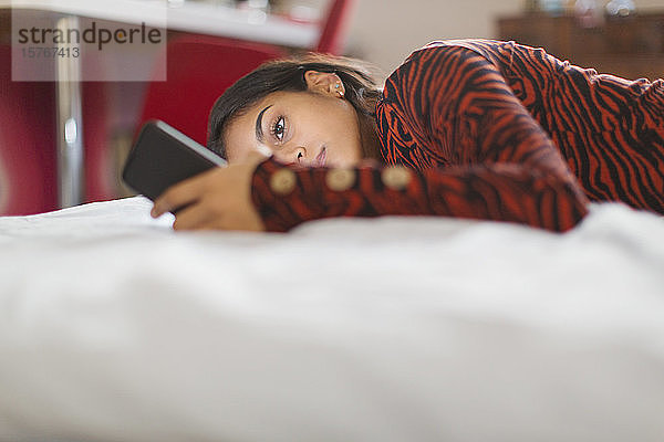 Konzentriertes Teenager-Mädchen mit Smartphone auf dem Bett liegend