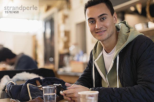 Porträt selbstbewusster junger männlicher Student  der ein Smartphone in einem Café benutzt