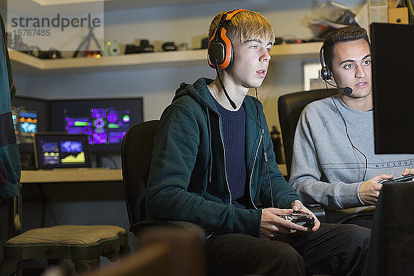 Teenager-Jungen mit Kopfhörern spielen ein Videospiel am Computer in einem dunklen Raum
