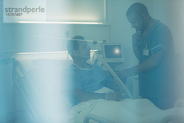 Krankenpfleger mit Stethoskop bei der Untersuchung eines Patienten im Krankenhausbett