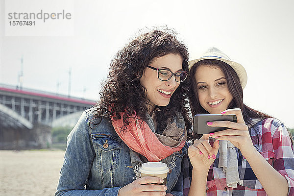 Junge Frauen  die ein Smartphone benutzen und im Freien Kaffee trinken