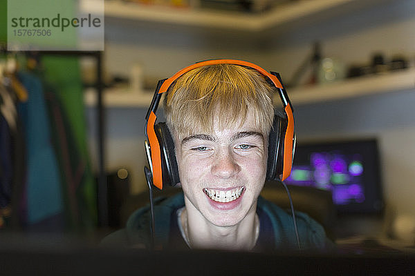 Glücklicher Teenager mit Headset  der ein Videospiel am Computer spielt