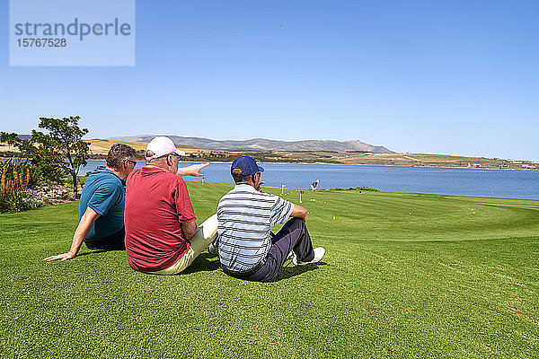 Männliche Golfer beim Entspannen mit Blick auf den See vom sonnigen Golfplatz aus