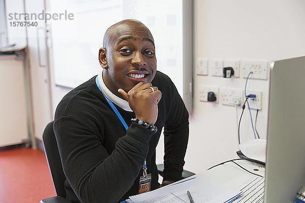 Porträt eines selbstbewussten männlichen Lehrers einer Volkshochschule am Computer im Klassenzimmer