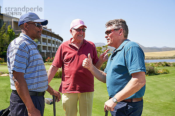 Glückliche männliche Golffreunde unterhalten sich auf einem sonnigen Golfplatz