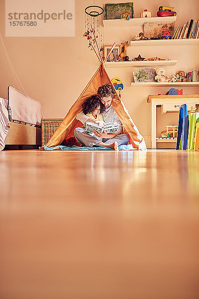 Vater und Tochter lesen ein Buch im Tipi