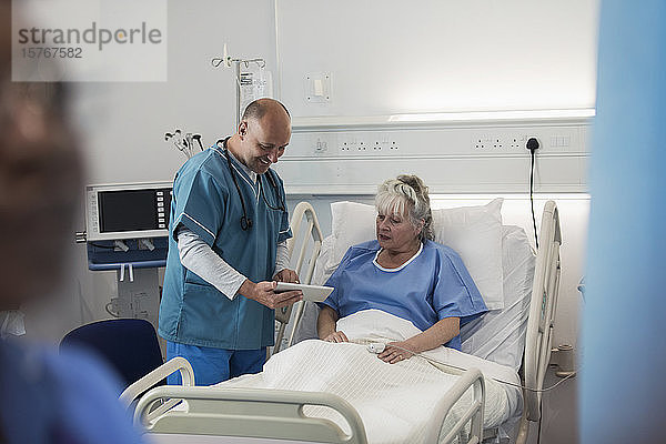 Arzt mit digitalem Tablet bei der Visite  Gespräch mit älterem Patienten im Krankenhauszimmer