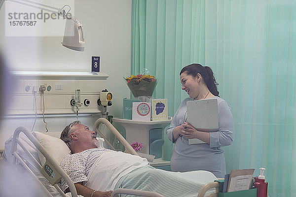 Arzt mit Krankenblatt im Gespräch mit älterem Patienten im Krankenhauszimmer
