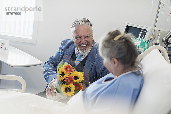 Glücklicher älterer Mann mit Blumenstrauß  der seine Frau im Krankenhaus besucht