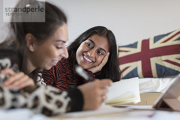 Lächelnde Teenager-Freundinnen  die auf dem Bett Hausaufgaben machen