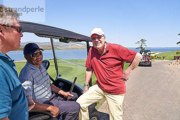 Glückliche männliche Golffreunde unterhalten sich am Golfwagen auf einem sonnigen Platz